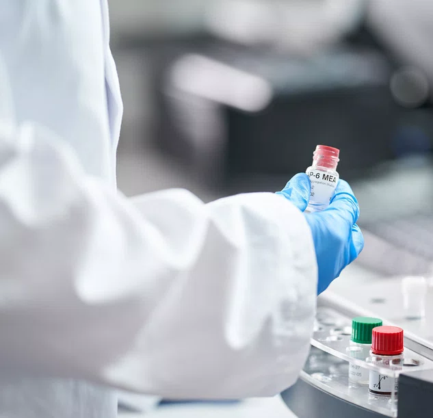 Lab assistant wearing a white lab coat and blue surgical gloves, holding a blood sample in a pot.